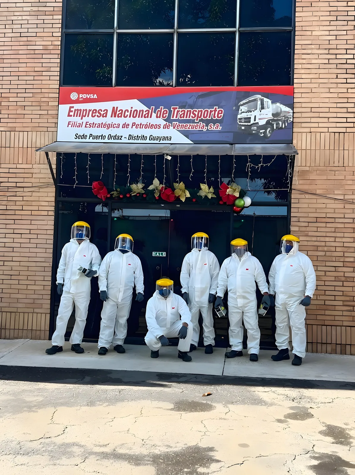 Seven workers in white coveralls and face shields in front of the building.