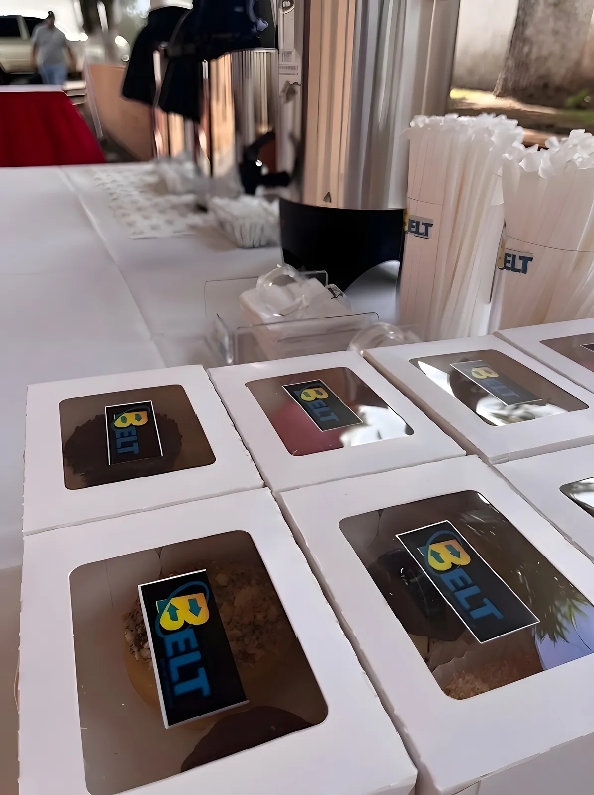 Desserts in white windowed boxes with a BELT label, in front of the coffee urns.